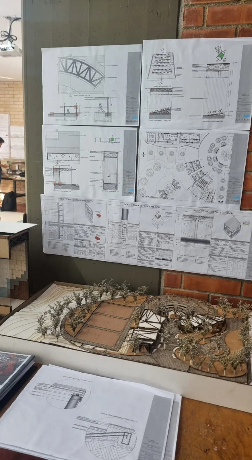 Láminas de planta, cortes y fichas técnicas de detalle exterior, intermedio e interior expuestas junto a la maqueta.