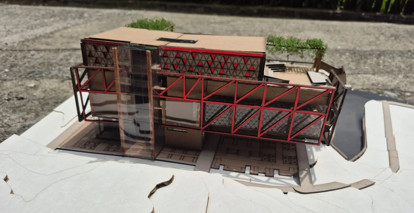 Maqueta del museo sobre la base del predio, con la celosía triangular y el voladizo estructural en rojo.